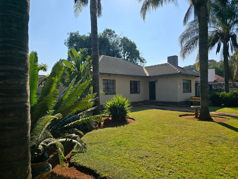 Front view of a single-story brick house featuring a tiled roof, security bars on windows, and a well-maintained front garden with mature palm trees.