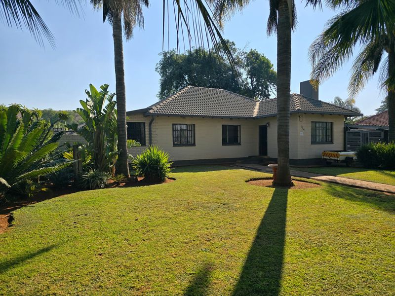 Front view of a single-story brick house featuring a tiled roof, security bars on windows, and a well-maintained front lawn with mature palm trees.