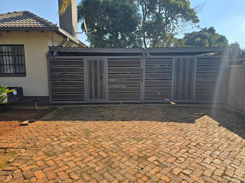 Front exterior view featuring a brick paved driveway, a modern horizontal slat sliding gate with integrated pedestrian door, and a tiled roof structure.