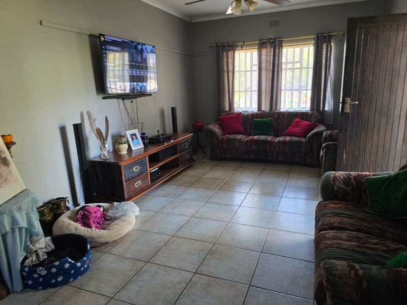 A living room featuring tiled flooring, a ceiling fan, and windows fitted with security bars.