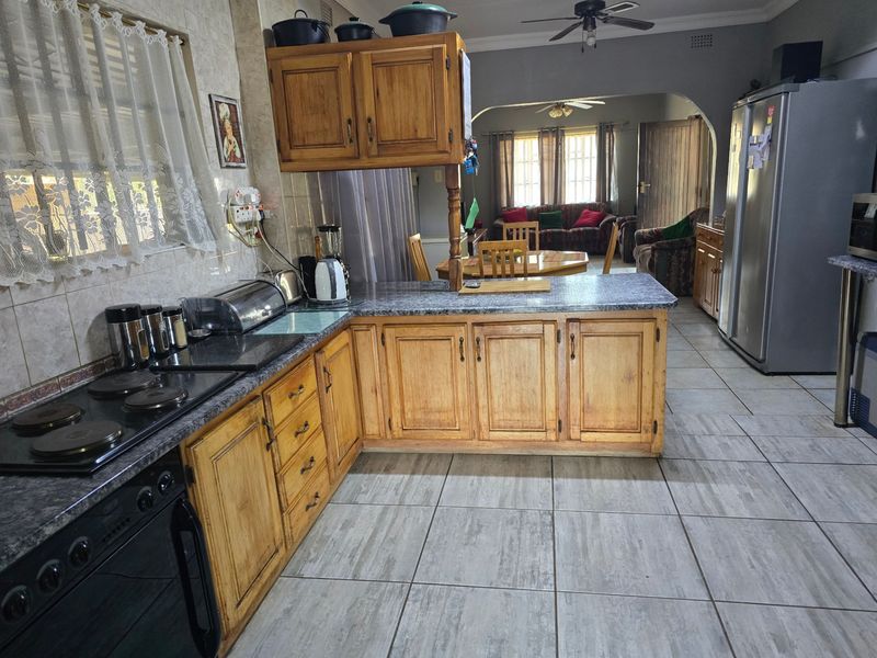 Open-plan kitchen and living area featuring wooden cabinetry, laminate countertops, built-in stove, and ceramic floor tiles, offering a functional layout with potential for modernization.