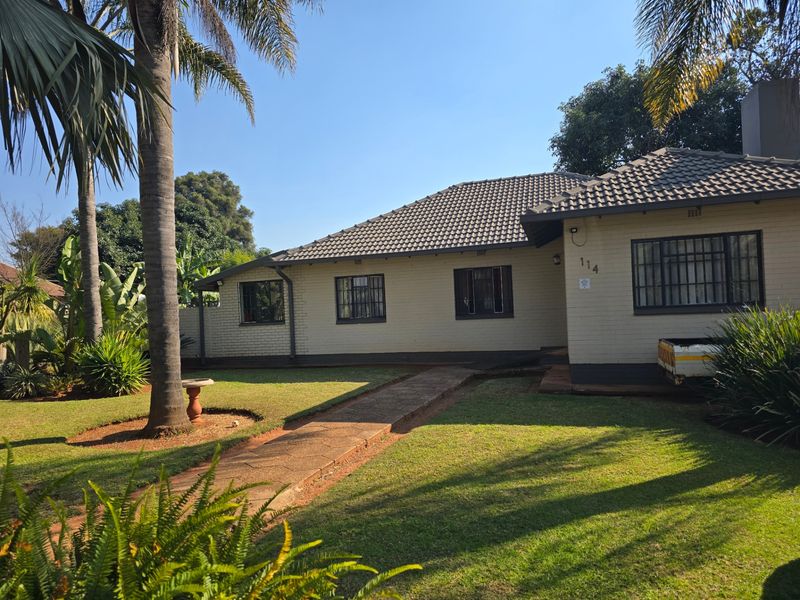 A well-maintained single-story brick house featuring a tiled roof, security bars on windows, and a neat front garden with a paved walkway.