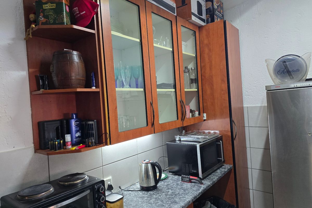 A functional kitchen area featuring wood-tone cabinetry with glass display sections, granite-look countertops, and a tiled splashback.