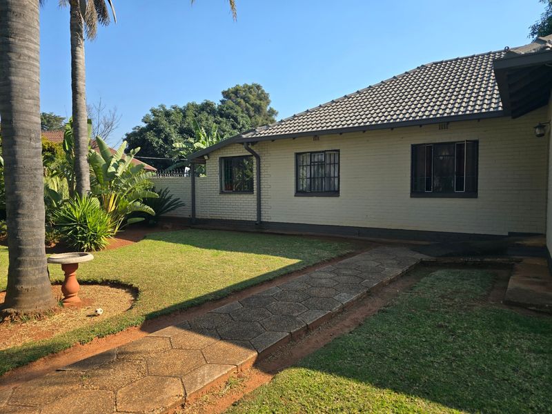 A well-maintained rear exterior view of the house featuring a brick facade, tiled roof, and a paved walkway leading through the garden.