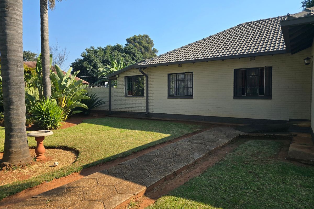 A well-maintained rear exterior view of the house featuring a brick facade, tiled roof, and a paved walkway leading through the garden.