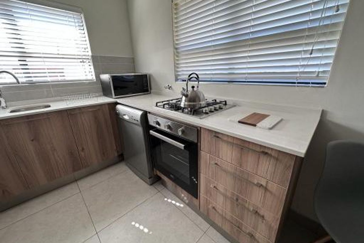 A modern kitchen featuring wood-finish cabinetry, stone countertops, a gas hob, built-in oven, and tiled flooring with ample natural light.