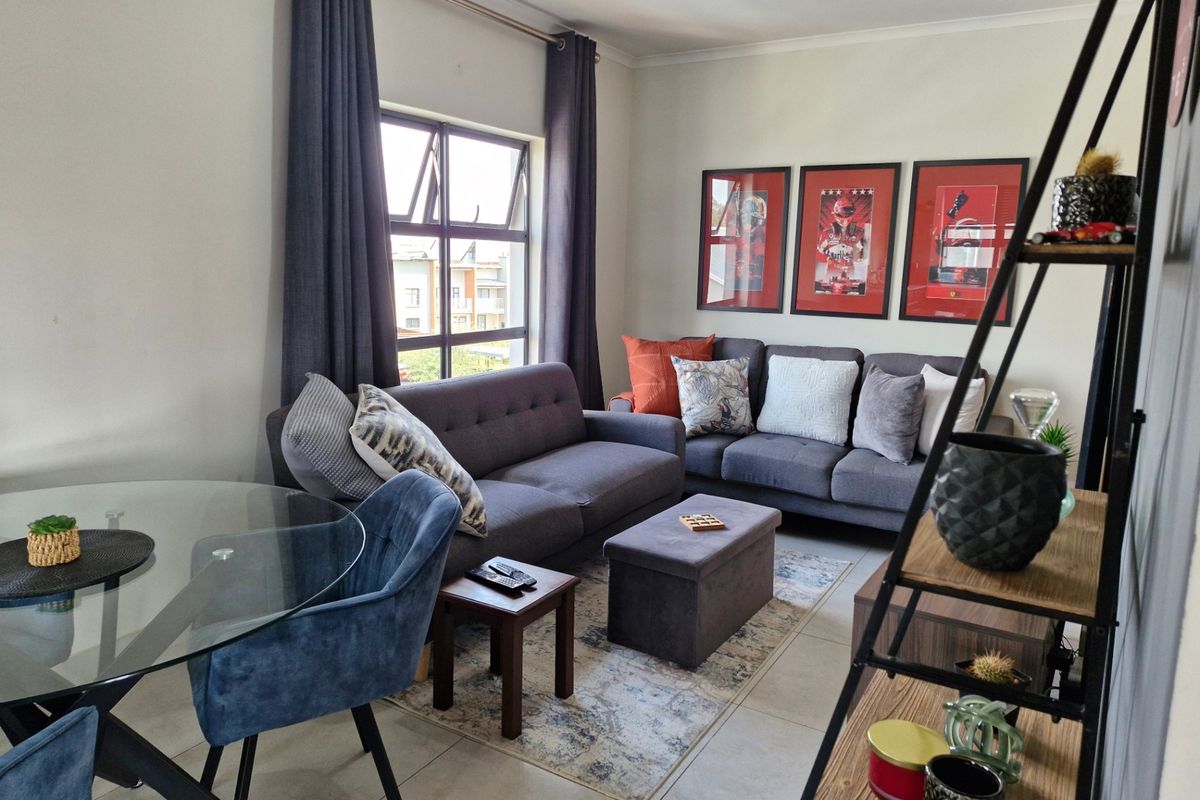 A well-lit open plan living and dining area featuring neutral tiled flooring and a large window providing natural light.
