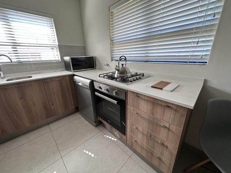 Modern kitchen featuring wood-finish cabinetry, stone countertops, a gas hob, built-in oven, and tiled flooring with ample natural light.