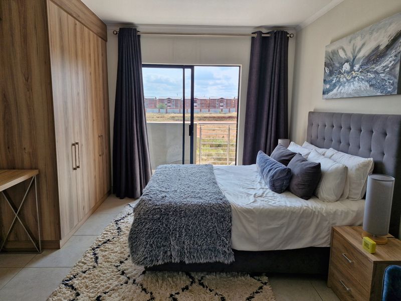 A well-maintained bedroom featuring built-in wooden wardrobes, tiled flooring, and a sliding glass door providing access to a private balcony.