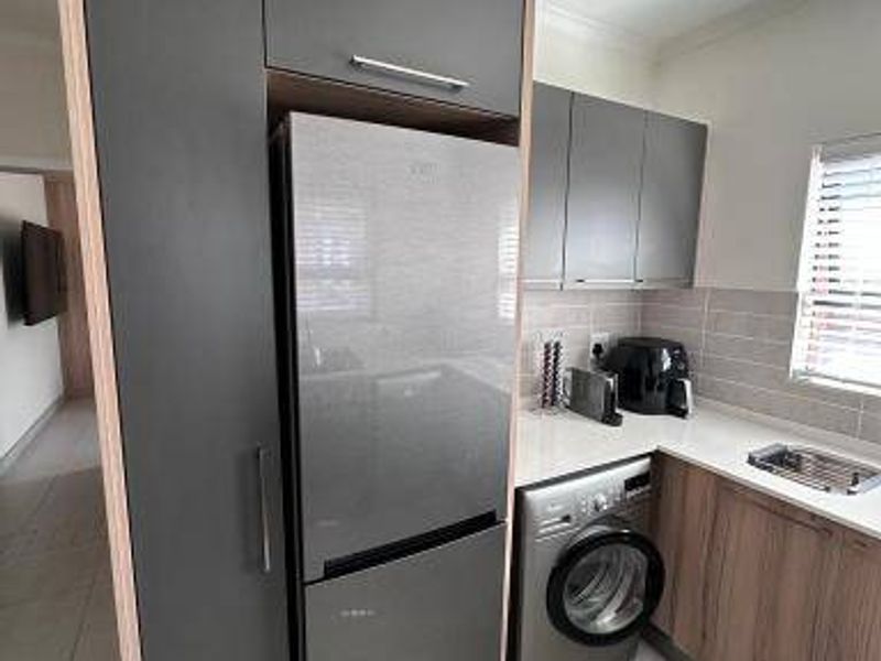 Modern kitchen featuring grey cabinetry, wood-look lower cupboards, integrated fridge space, and an under-counter washing machine with a tiled backsplash.