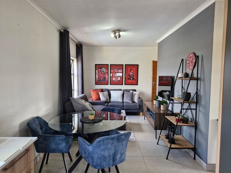 An open-plan living and dining area featuring tiled flooring, a neutral color palette, and a grey accent wall.