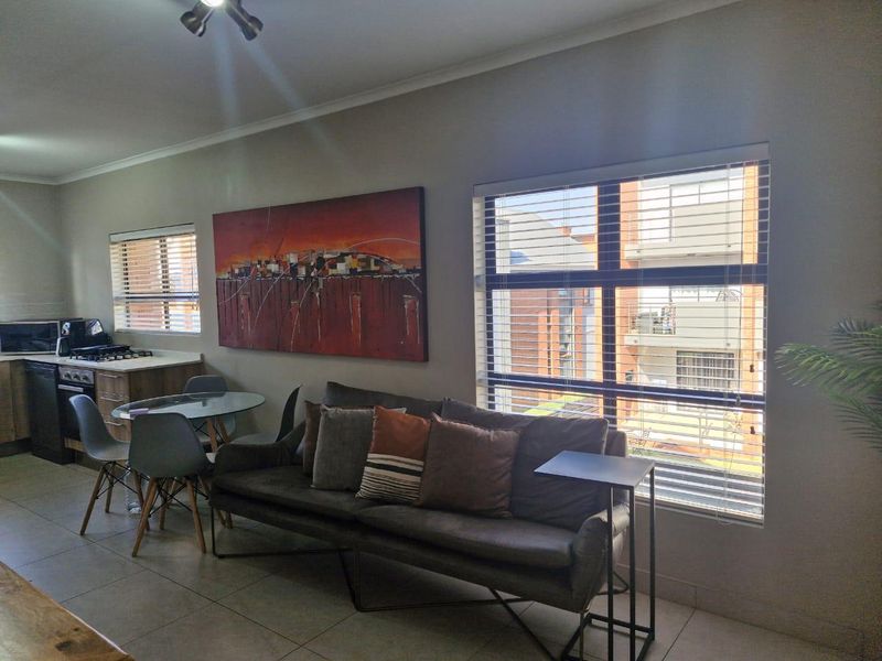 Open-plan living and kitchen area featuring tiled flooring, large windows with venetian blinds, and functional built-in kitchen cabinetry with integrated appliances.