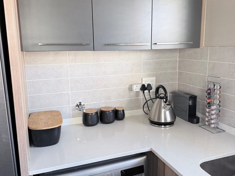 Modern kitchen area featuring sleek grey cabinetry, stone countertops, subway tile backsplash, and an integrated washing machine.