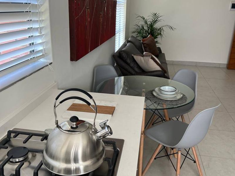 Open plan kitchen and dining area featuring a gas hob, stone countertops, and neutral tiled flooring with large windows and venetian blinds.