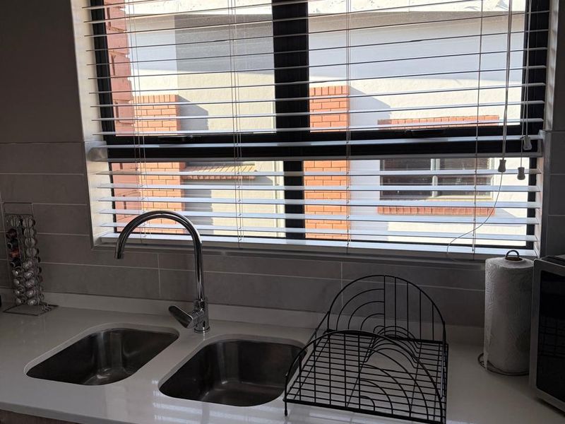 A modern kitchen sink area featuring a double bowl stainless steel sink, chrome mixer tap, stone countertops, and light wood-look cabinetry.