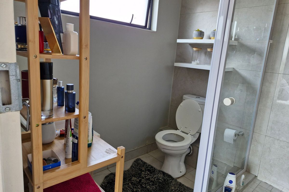 A functional bathroom featuring a glass-enclosed shower, a standard toilet, and built-in wall shelving with neutral tiled finishes.