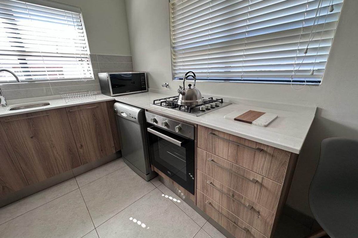 Modern kitchen featuring wood-finish cabinetry, stone countertops, a built-in gas hob, oven, and tiled flooring with ample natural light from dual windows.