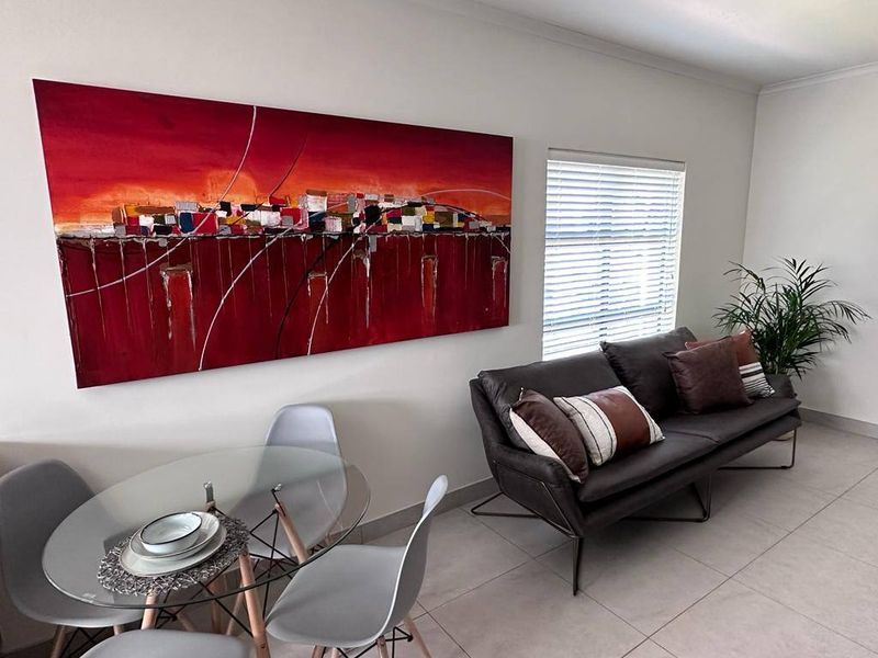 A bright open-plan living and dining area featuring neutral tiled flooring and modern venetian blinds.