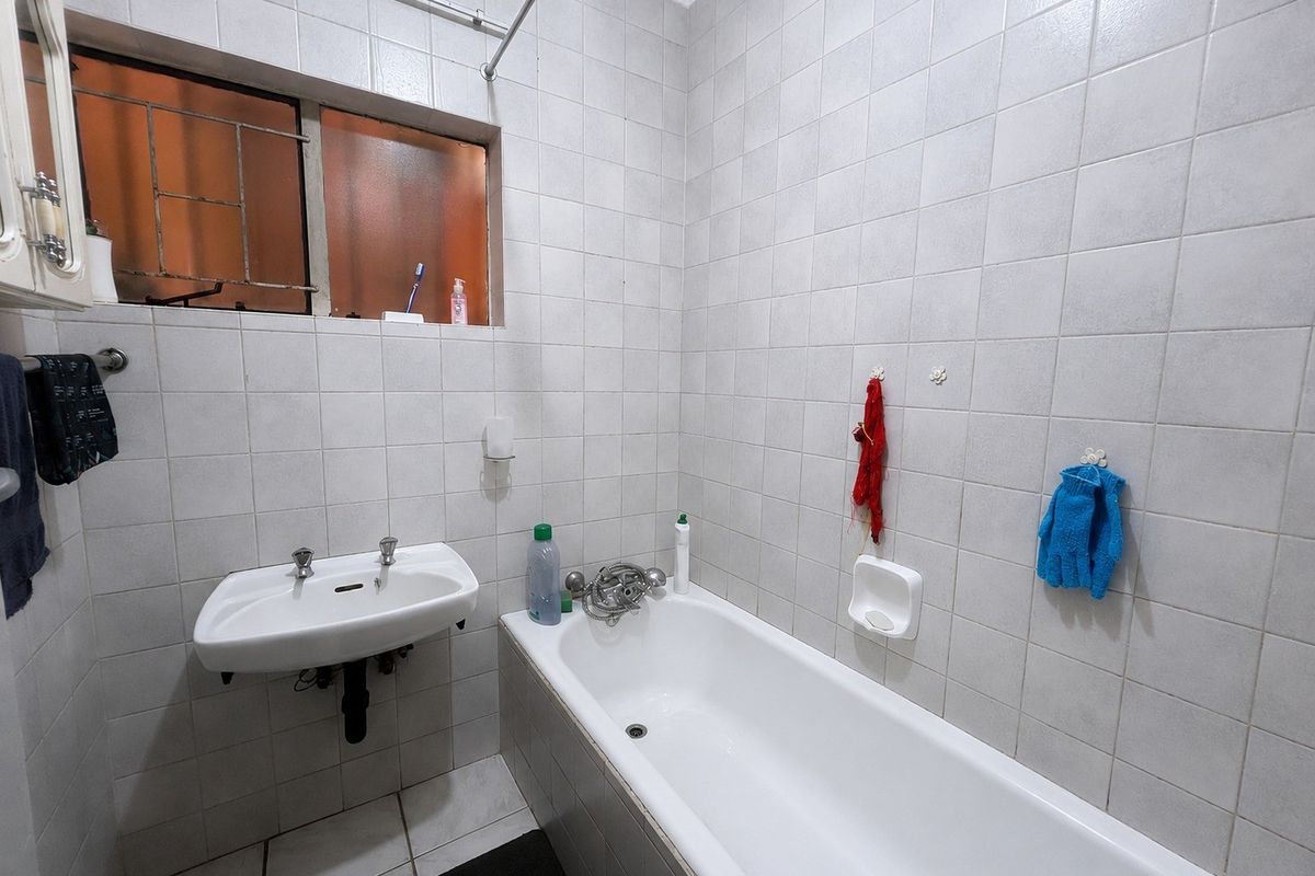 A functional bathroom featuring a wall-mounted basin, a built-in bathtub, and full-height wall tiling. The space is ready for modernization.
