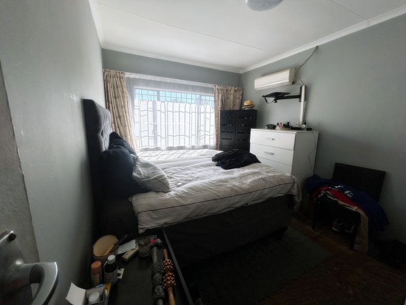 A functional bedroom featuring a wall-mounted split-system air conditioner and large window with curtain tracks.