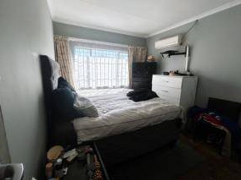 A functional bedroom featuring an installed air conditioning unit and security bars on the window, providing a basic and practical living space.