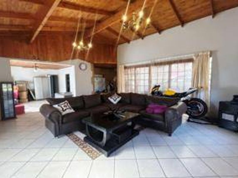 Spacious living room featuring high exposed timber beam ceilings, tiled flooring, and large windows providing natural light.