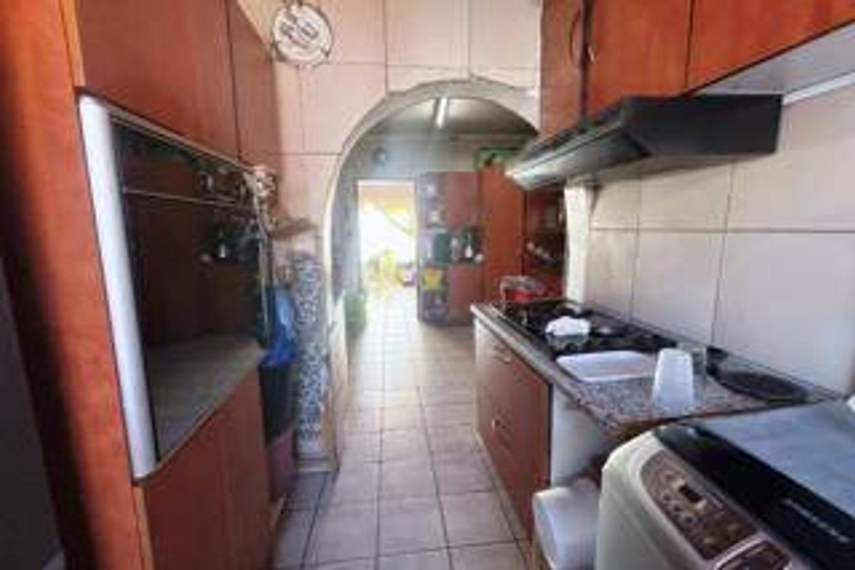 A functional kitchen featuring built-in cabinetry, a gas hob with extractor fan, built-in oven, and tiled flooring, leading through an archway to an adjacent space.