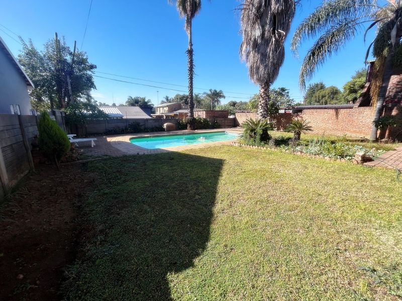 A private backyard featuring a swimming pool, paved surround, and established garden area enclosed by brick boundary walls.