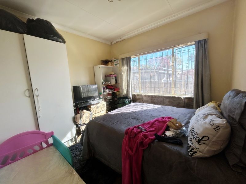 A bedroom featuring a large window with security bars and ceiling cornice detailing, currently showing signs of wear and water damage on the ceiling.