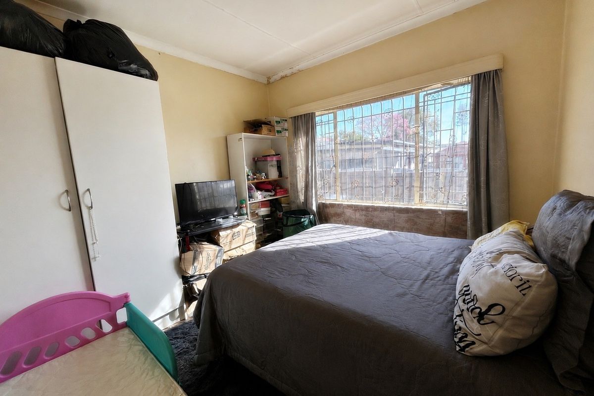 A bedroom featuring security bars on the window and a built-in wardrobe, showing signs of ceiling wear and water staining.