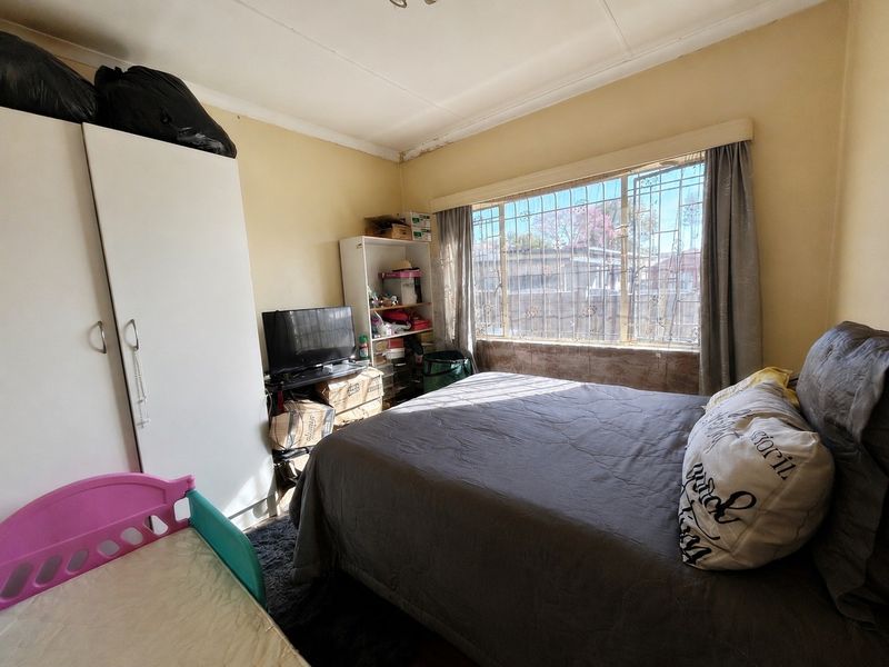 A bedroom featuring security bars on the window and a built-in wardrobe, showing signs of ceiling wear and water staining.