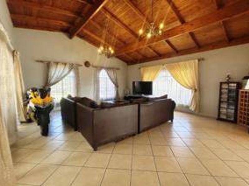 Spacious living room featuring a high vaulted timber ceiling, ceramic tiled flooring, and large windows allowing for ample natural light.