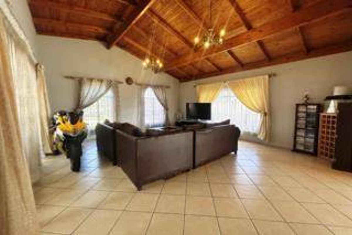 Spacious living room featuring a high vaulted timber ceiling, ceramic tiled flooring, and large windows allowing for ample natural light.