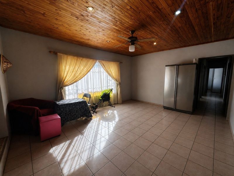 Spacious living area featuring tiled flooring and a warm timber tongue and groove ceiling with integrated downlights and a ceiling fan.