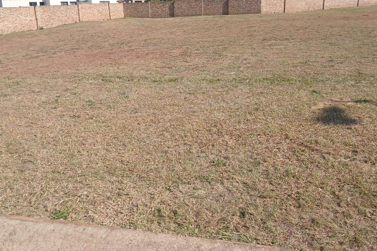 A vacant residential plot featuring a level grass surface enclosed by a secure perimeter brick wall.