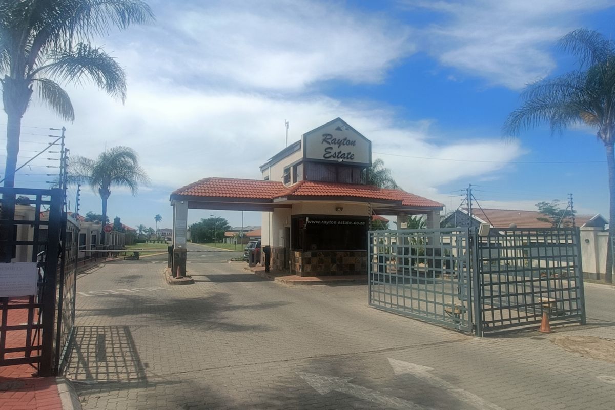 The main entrance gate and guard house of Rayton Estate, featuring paved access, security fencing, and a tiled roof structure.