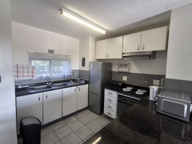 Functional kitchen featuring granite countertops, built-in oven with hob, extractor fan, and ample cabinetry, finished with tiled flooring.