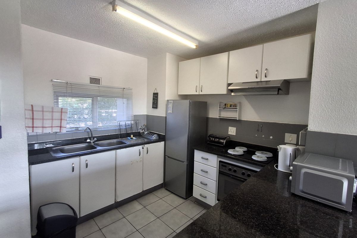 Functional kitchen featuring granite countertops, built-in oven with hob, extractor fan, and ample cabinetry, finished with tiled flooring.