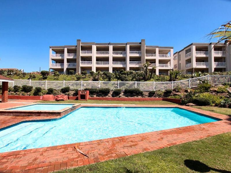 Communal swimming pool area featuring brick paving, a built-in braai, and landscaped gardens set against the apartment complex.