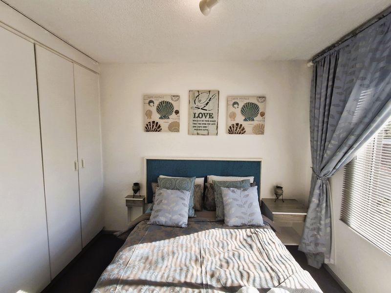 A cozy bedroom featuring a built-in wardrobe, neutral walls, and venetian blinds, providing a functional and comfortable sleeping space.