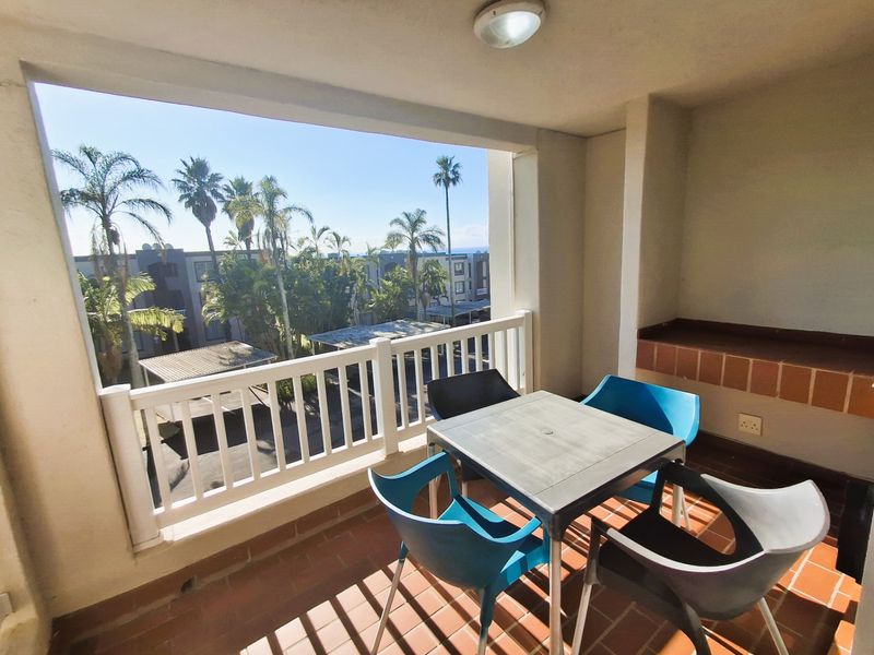 A covered balcony featuring a built-in braai, tiled flooring, and a white balustrade, offering an outdoor space for relaxation and entertaining.