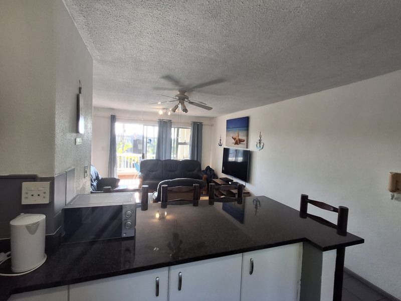 Open plan living area featuring a kitchen with granite countertops and cabinetry, flowing into a lounge space with access to a balcony.