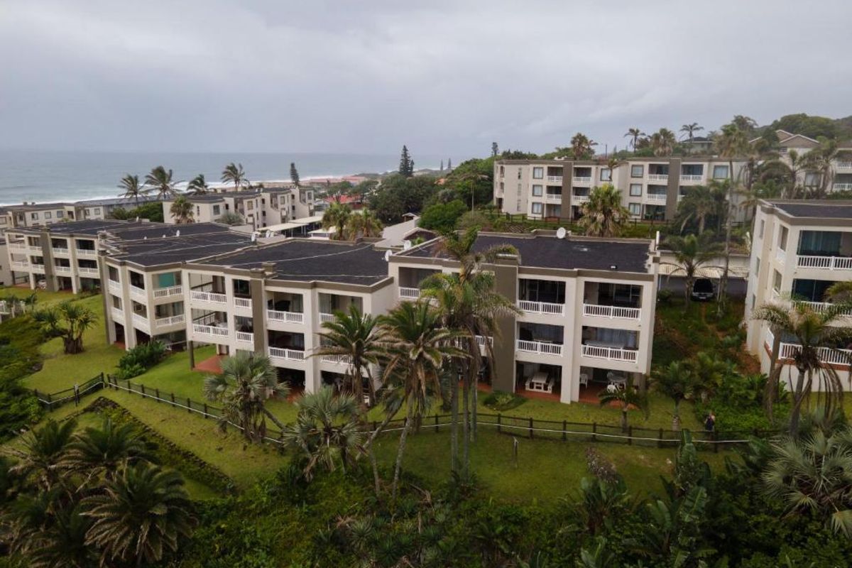 Aerial view of a coastal apartment complex featuring multi-story buildings, private balconies, and well-maintained landscaped gardens near the ocean.