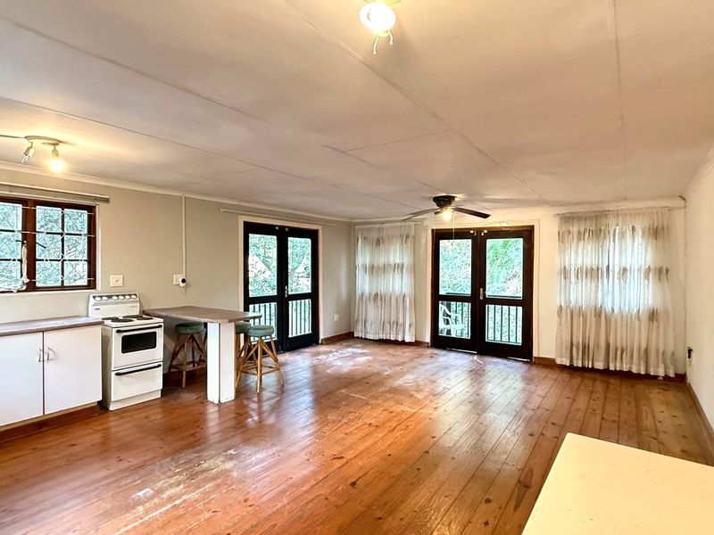 Open-plan living area featuring timber flooring, a functional kitchen with a breakfast bar, and double doors leading to an outdoor space.