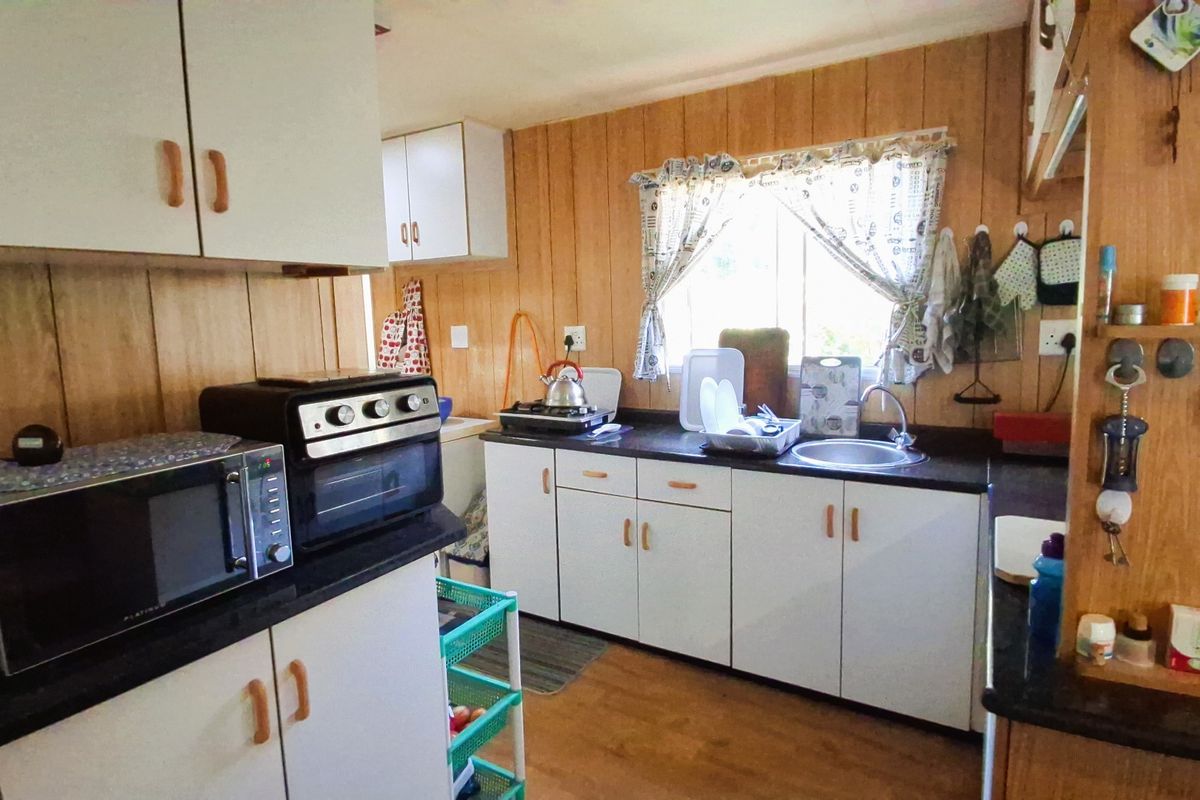 A functional kitchen featuring wood paneling, white cabinetry, and dark laminate countertops, offering a dated aesthetic with potential for modern renovation.