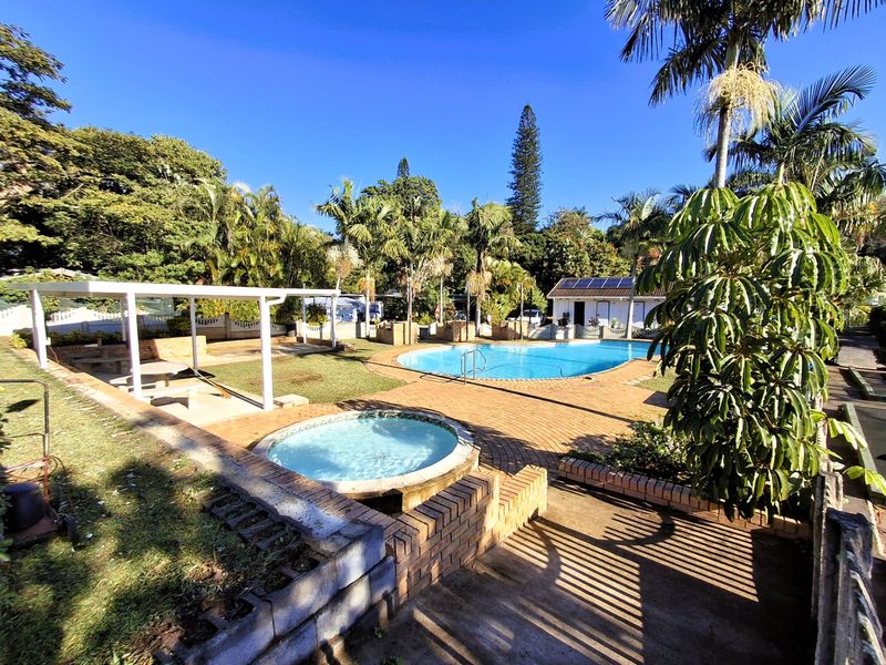Outdoor communal pool area featuring a swimming pool, integrated jacuzzi, brick paved surround, and a covered patio structure.