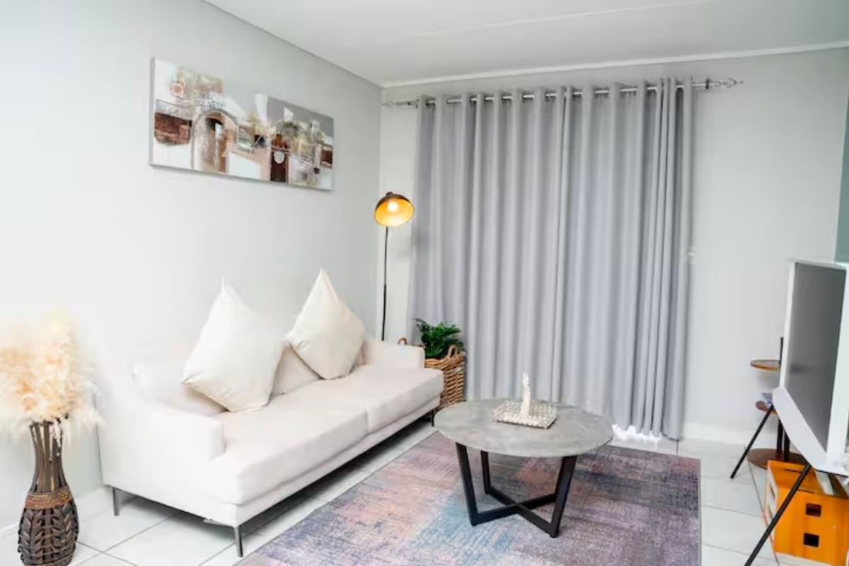 A well-maintained living room featuring neutral wall tones, tiled flooring, and floor-to-ceiling curtains providing access to the exterior.