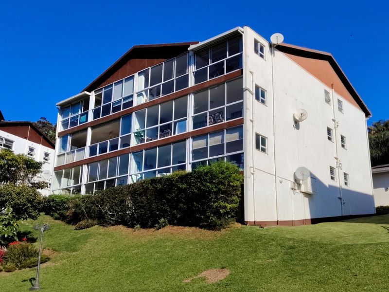 Exterior view of a multi-story apartment building featuring enclosed balconies, white facade, and well-maintained surrounding lawn area.