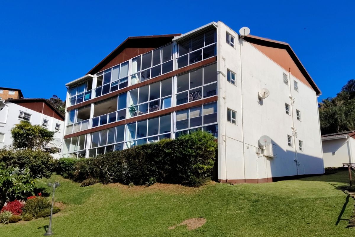 Exterior view of a multi-story apartment building featuring enclosed balconies, white facade, and well-maintained surrounding lawn area.