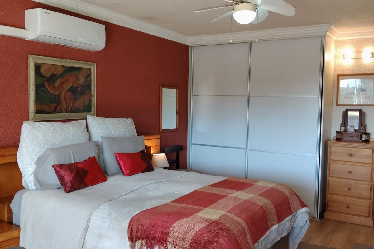 A bedroom featuring a built-in sliding wardrobe, ceiling fan, and wall-mounted air conditioning unit, finished with laminate flooring and decorative coving.